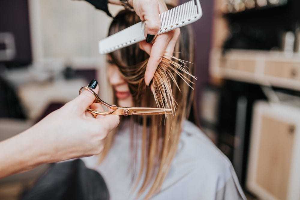 Close-up of a hairstylist trimming a client's hair with scissors and a comb in a salon.