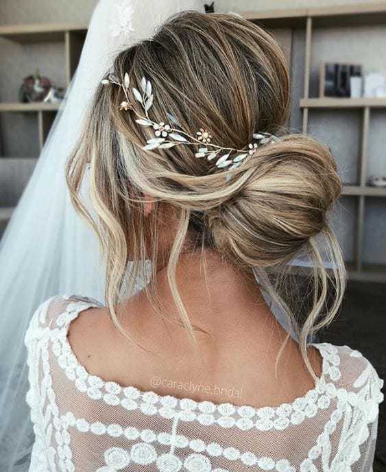 Bride with low bun hairstyle adorned with floral hair accessory, wearing a lace wedding dress.